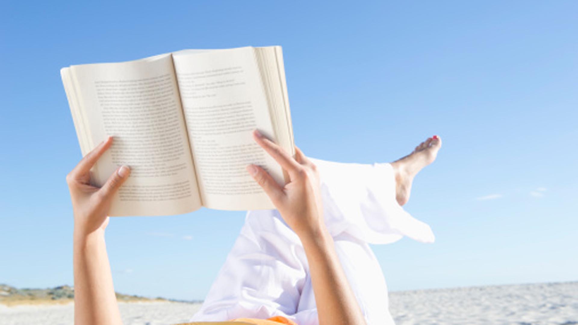 Mixed race woman reading book on beach